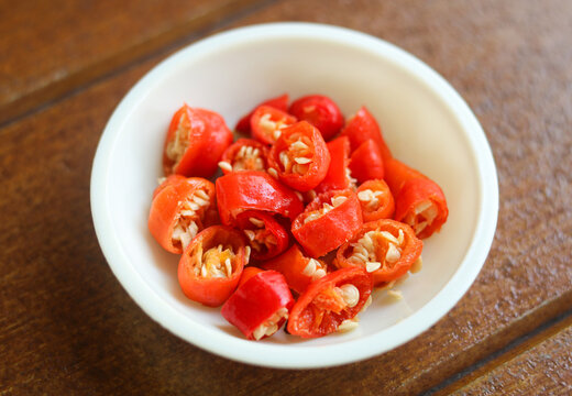 A closeup shot of freshly sliced red chilies served in a small white ceramic bowl. The vibrant red chili segments are cut into bite-sized rounds.