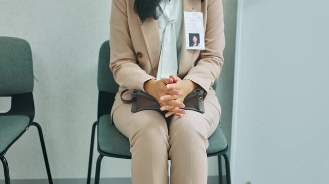 Professional woman with ID badge waiting in an office lobby, hands clasped. Concept of job interview, business meeting, or corporate anticipation.