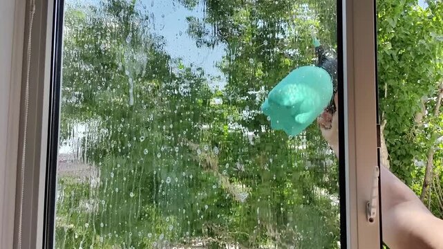 Manual window spraying with soapy water, routine apartment maintenance, home maintenance, spring cleaning
