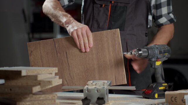 Person holding wooden board near cordless drill and guide jig on workshop table. Woodworking, carpentry and furniture assembly concept.