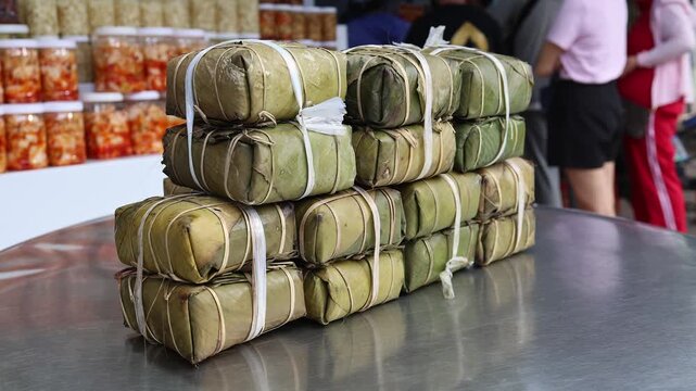 Traditional Vietnamese Banh Tet rice cakes wrapped in banana leaves for sale. Close-up of stacked Lunar New Year holiday food on a market display counter in Vietnam.