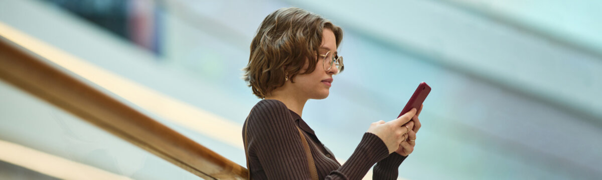 Website header shot of young adult Caucasian woman using smartphone while standing on escalator, checking messages in transit. Ideal for digital communication, mobile lifestyle, commuting concepts