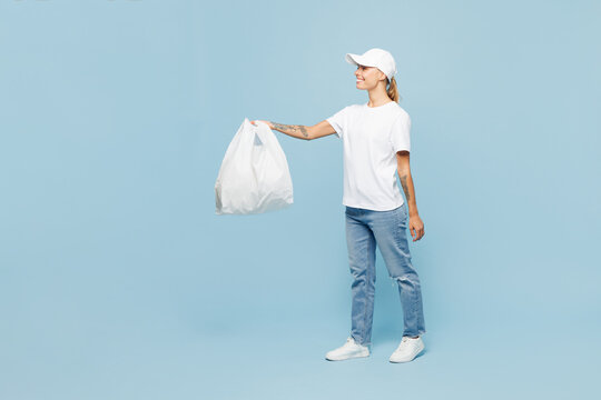 Full body delivery employee woman wear white cap T-shirt uniform workwear work as dealer courier hold plastic food bag from shop advert area isolated on plain blue background studio. Service concept.