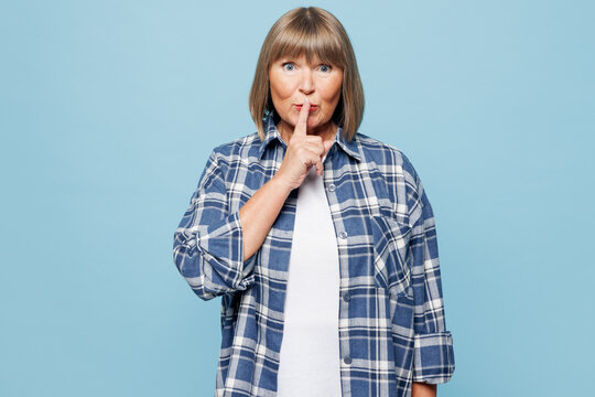 Elderly secret blonde woman 50s years old in checkered shirt casual clothes say hush be quiet with finger on lips shhh gesture isolated on plain pastel light blue background studio Lifestyle concept