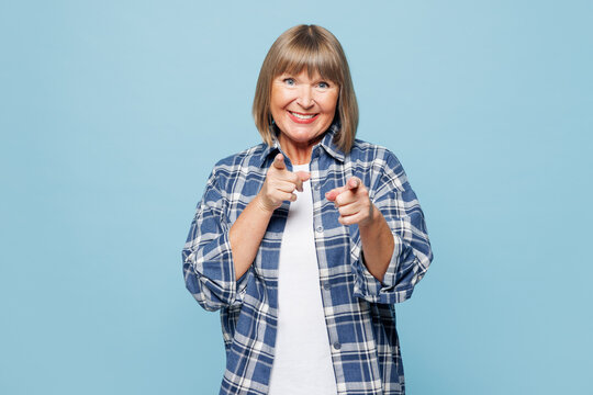 Elderly blonde woman 50s years old wears checkered shirt casual clothes point index finger camera on you motivating encourage isolated on plain pastel light blue background studio. Lifestyle concept.