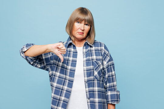 Elderly disappointed blonde woman 50s years old wear checkered shirt casual clothes showing thumb down dislike gesture isolated on plain pastel light blue background studio portrait Lifestyle concept