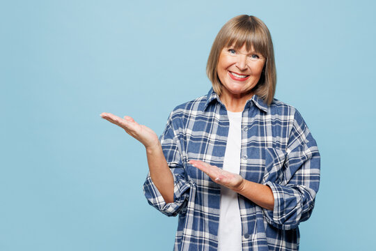 Elderly happy blonde woman 50s years old wear checkered shirt casual clothes point index finger aside on area mock up isolated on plain pastel light blue background studio portrait. Lifestyle concept.