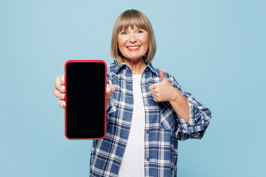 Elderly blonde woman 50s years old wear checkered shirt casual clothes hold in hand use point on blank screen mobile cell phone isolated on plain pastel light blue background studio Lifestyle concept