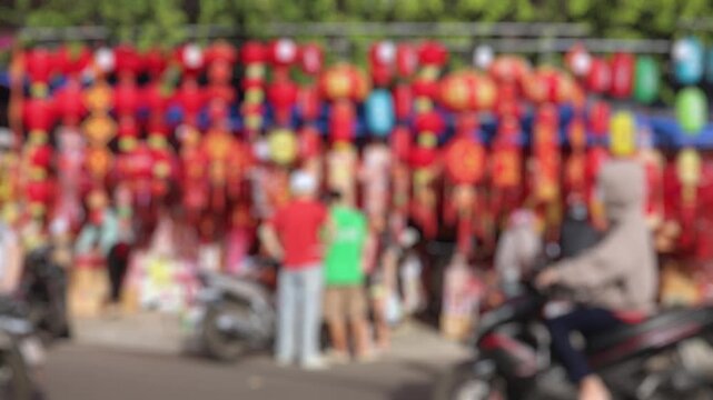 Bokeh view of Vietnamese people buying traditional red lanterns and lucky ornaments at a festive street market before Tet holiday. Lunar New Year shopping concept. Blurred background footage.