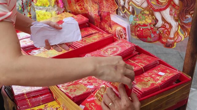 Hand of a street vendor sorting lucky red envelopes for Tet at a market stall. Close-up of traditional Vietnamese Li Xi money packets for Lunar New Year celebration.