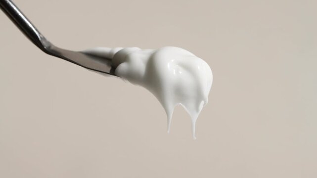 White hand and face cream dripping from a spatula close-up, beige background.