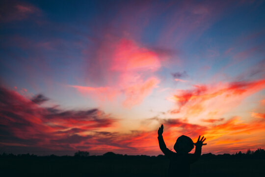 Young Boy Reaching for Sky with Colorful Sunset