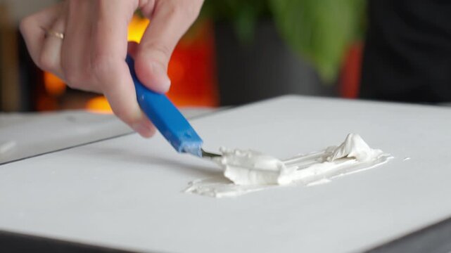 A hand spreads white texture paste on a canvas or panel with a small spatula. DIY art, handmade decor and creative hobby concepts