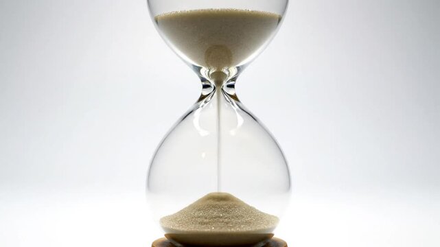 Close up view of hourglass with sand trickling from top to bottom, representing passing time