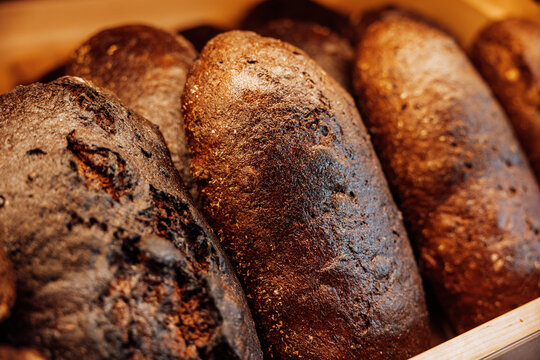 Close-up of dark rye bread loaves with glossy crusts displayed in a warm wooden bakery shelf, highlighting rustic texture and artisan baking
