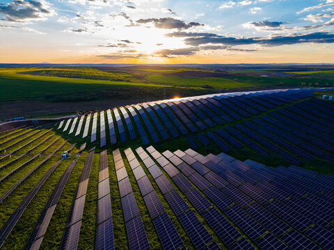 Solar panels stretch across a large field at sunset with clouds in the sky and green hills in the background
