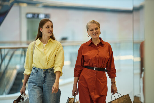 Caucasian young adult woman and senior woman carrying shopping bags and walking through mall, representing retail spending and family lifestyle. Ideal for consumer marketing and sales campaigns