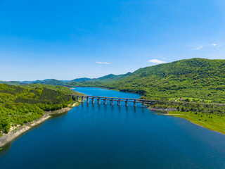 Obraz premium Clear blue water flows under the bridge surrounded by green hills and blue sky in a scenic view of nature and landscape in the daytime