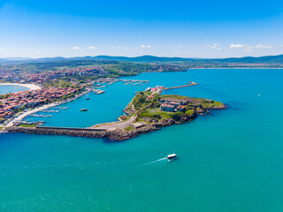 Fototapeta premium Bright day over a coastal town with a marina, boats, and green land by the water, showing a clear blue sky and hills in the background