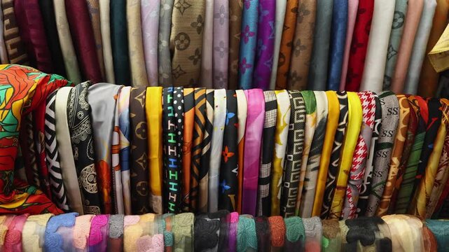 Colorful silk scarfs for sale at an outdoor street market in Nha Trang, Vietnam. Close-up of traditional Vietnamese fabric shawls with patterns displayed on a rack for tourists and local shoppers.