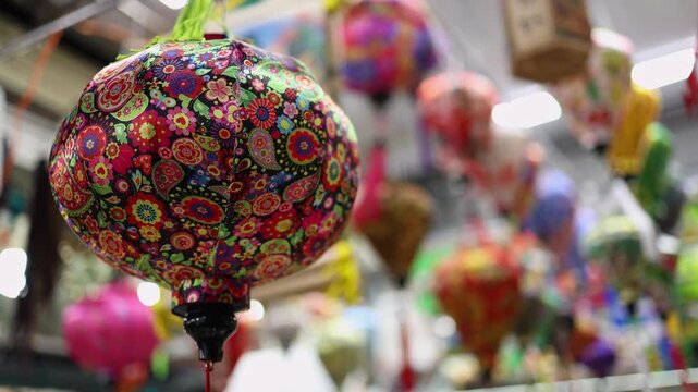 Traditional souvenir lanterns for sale at a Vietnamese street shop in Vietnam. Close-up of colorful oriental fabric lanterns with floral patterns hanging at a local market. Asian cultural footage.