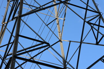 Fototapeta premium Metal lattice towers stretch toward the clear blue sky. Structural beams form intricate geometric patterns. Industrial strength contrasts with serene atmosphere. Ideal for energy, infrastructure