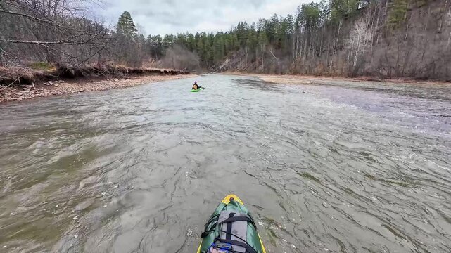 Wide downstream approach with distant paddler in green kayak, expansive river surface, tree lined banks and eroded cliff edges, calm scouting mood as kayaker glides through steady current