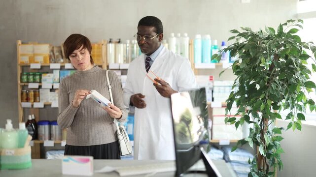  Woman choose buy gel for burns at pharmacy, compare with other good. Client check for absence of harmful substances, view product in details. African man pharmacist offer available assortment item