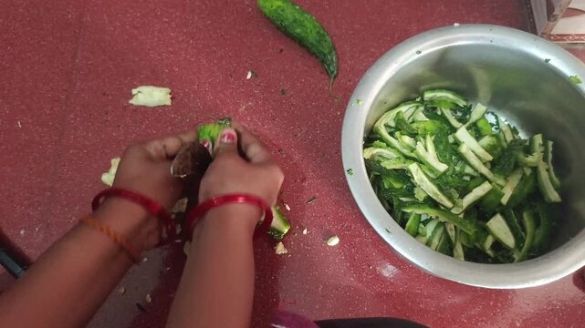 Top view of woman hands cutting fresh bitter gourd near a steel bowl filled with green karela slices