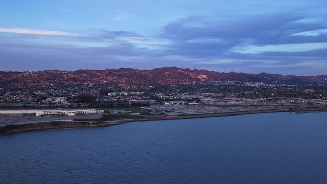 Majestic aerial view flying over the San Francisco bay towards the city of Albany and the Berkeley hills, with the last rays of sunlight illuminating the landscape during a colorful sunset