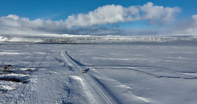 Aerial view of a lone car crossing the frozen landscape of Kleifarvatn on Iceland&rsquo;s Reykjanes Peninsula, with snowfields, volcanic terrain, and bright winter light.