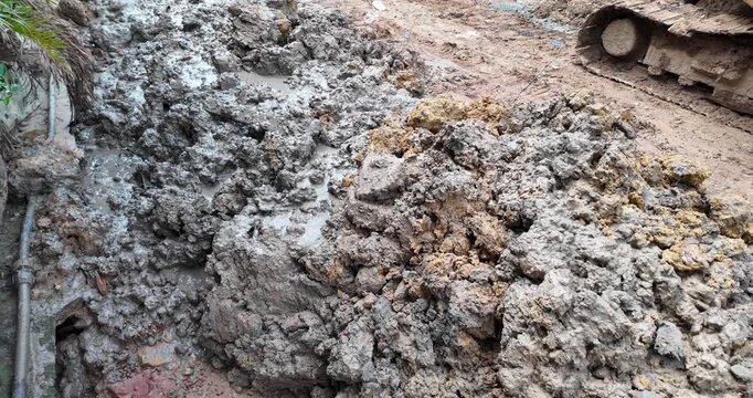 Close up of wet, muddy excavated earth next to an excavator's muddy tracks as it reverses over wet, cracked earth at an active construction site