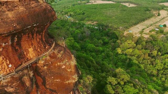 Aerial Push In of Wooden Walkway Red Rock Plateau of Wat Phu Tok Naga Temple, Lush Green Forest Below Thailand. Ideal for nature documentaries or travel content.