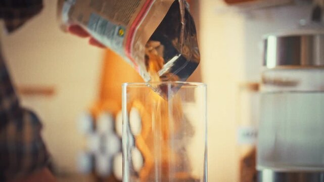 In her kitchen, a housewife pours a mix of assorted nuts into a clear glass jar, arranging a healthy snack. This tidy act underscores her focus on nutritious, convenient food preparation