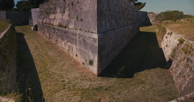 Corner stone wall with grassy passages beside fortification walls at Pula Castle.