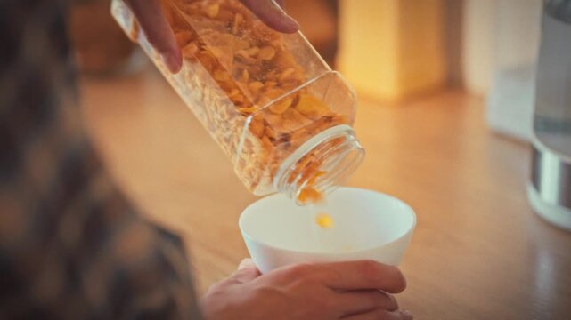 In bright morning kitchen, woman's hands scoop measured corn flakes into bowl, sunlight streams through window, embodying home cooking routines that promote balanced nutrition and healthy lifestyle