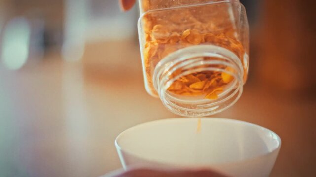 In home kitchen, woman's hands carefully pour yellow cornflakes into clean white bowl, preparing a nutritious breakfast. This simple act embodies the concept of healthy eating and mindful health care