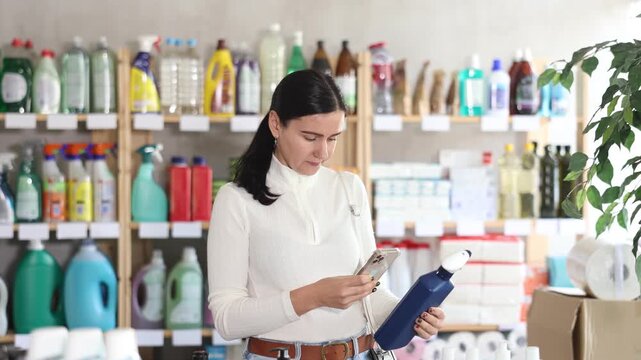 Middle-aged European woman stares intently at the screen of her mobile and scans the barcode on the spray packaging. Buyer pays for her purchases using a qr code. High quality 4k footage