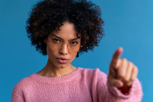 Focused young woman with curly hair pointing at camera in pink sweater with glasses for assertive portrait and recruitment banner