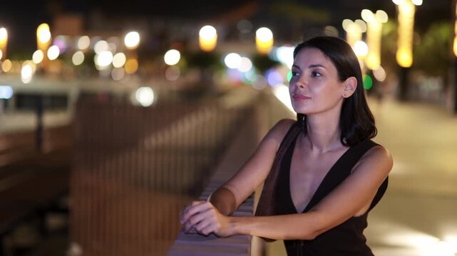 Elegant young woman leaning on parapet at Barceloneta beach promenade in summer evening