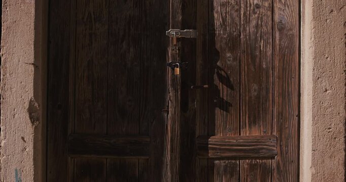 Close-up view of an old wooden door with metal lock and sunlight shadows.