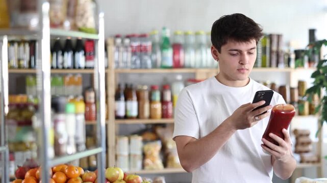 Before buying ketchup, young man scans barcode QR code on label of catsup package bottle, follows link and studies information for consumer in supermarket application
