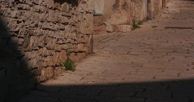 Stone alleyway with weathered wall and sunlight shadows in an old town.