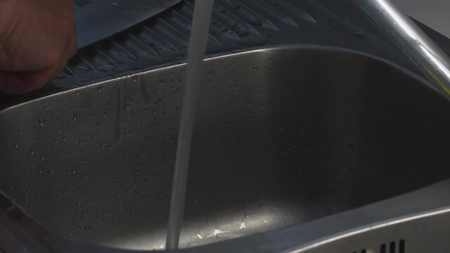 Man cleans various kitchen knives in sink while ensuring proper maintenance and hygiene techniques
