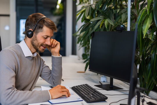 Support service operator talking to customer sitting at desk wearing headset working in modern open space office using PC computer