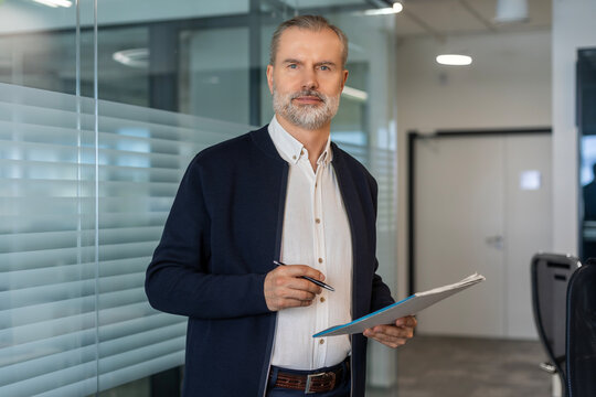 Smiling handsome businessman manager standing in office with documents