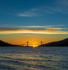Obraz premium Sunset view with suspension bridge over calm water