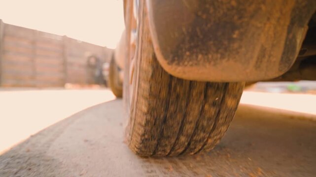 Low angle close-up of dirty car wheel and mud flap on road in golden light