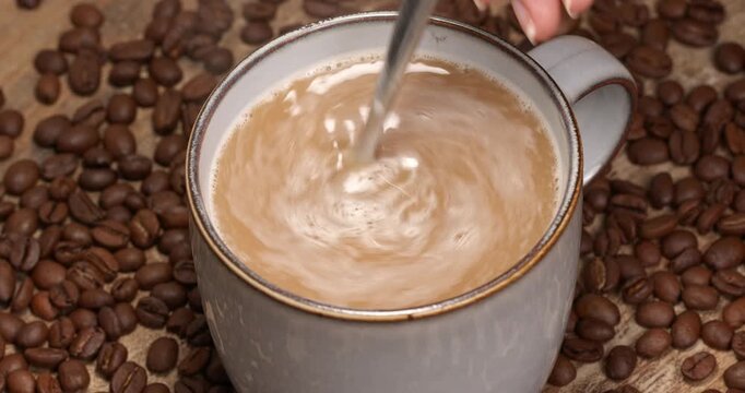 Hot instant coffee mix 3 in 1 being stirred in a cup close-up footage on a background of coffee beans.
