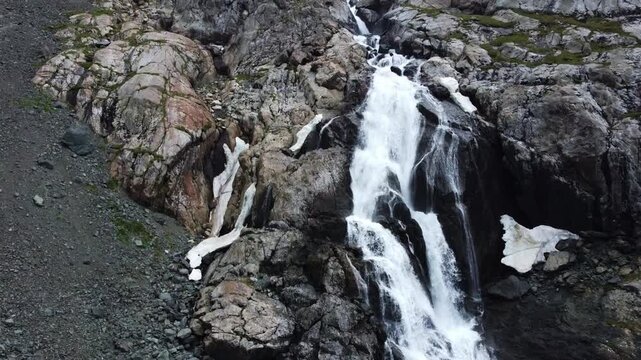 Close up aerial view of powerful mountain waterfall with melting snow patches on rugged cliffs, Ala-Kul, Kyrgyzstan, Karakol. High quality 4k footage